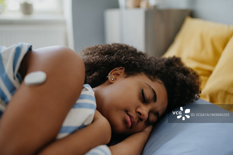 患有糖尿病的少女白天感到疲倦，小睡片刻以恢复精力。肩上戴着持续血糖监测仪的少女在床上睡觉图片素材