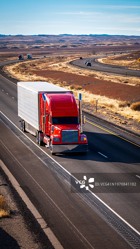 在阳光明媚的冬日下午，一辆红色半挂卡车在I-70公路上向东行驶的竖版照片图片素材