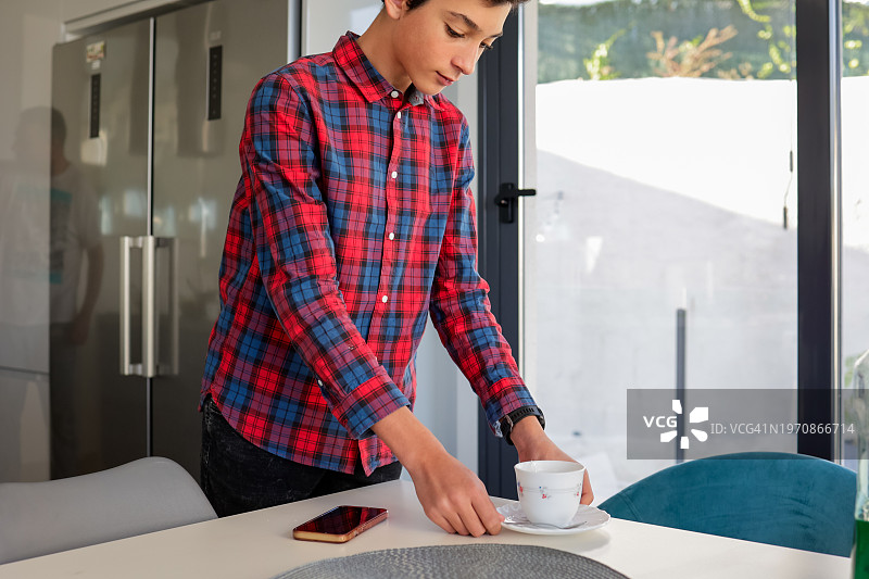 青少年在阳光明媚的厨房里把茶杯放在桌子上图片素材