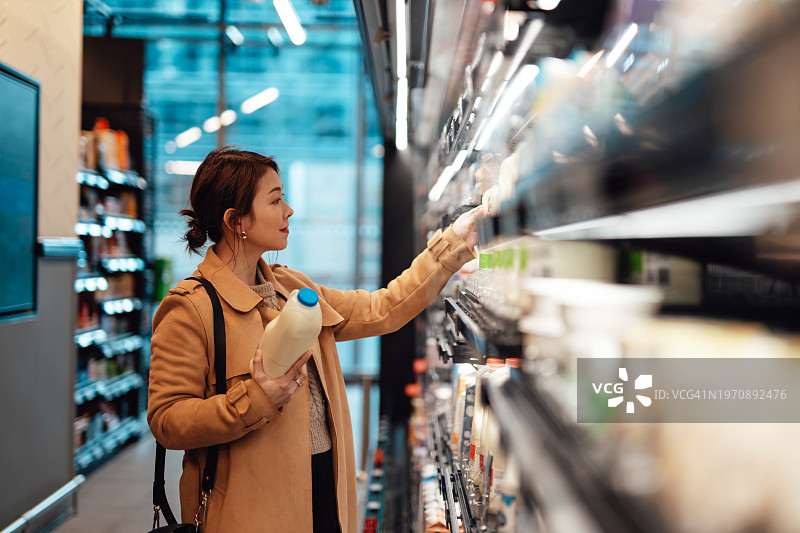 年轻的亚洲女人在超市货架上挑选新鲜有机牛奶图片素材