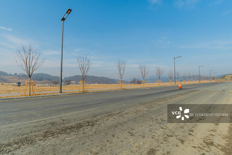 韩国建筑工地上的铺砌道路，有新种植的树木和新的路灯图片素材