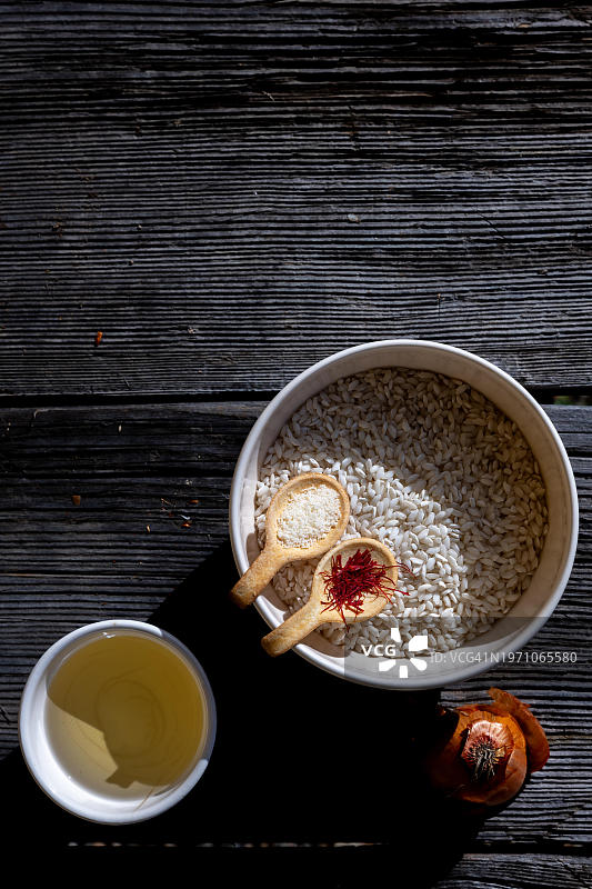 用于制作藏红花米饭的未经烹煮的食材，米兰风味烩饭配帕尔马干酪、白葡萄酒和洋葱，位于瑞士提契诺卢加诺的古老木桌上图片素材
