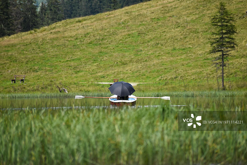 在奥地利施蒂里亚州施拉德明陶恩山区的斯特里舍康斯坦茨湖山间湖泊上，撑着阳伞在划艇上的度假者图片素材