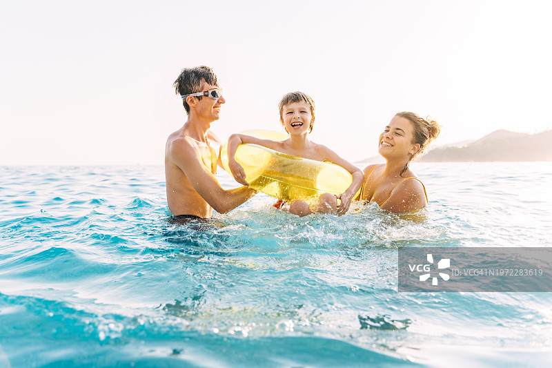 快乐的一家人和戴着游泳圈的小儿子在海里嬉戏图片素材