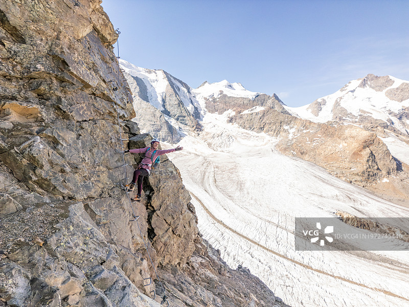 女人在阿尔卑斯山高空冰川之上的铁索攀岩路线上攀登图片素材