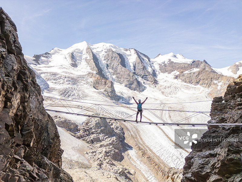 在阿尔卑斯山上徒步旅行，穿过冰川之上的悬索桥的女人图片素材