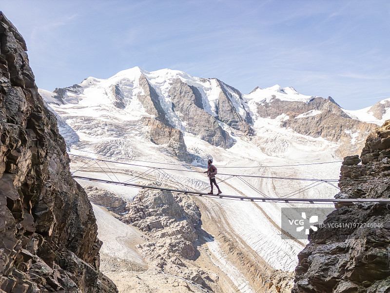 在阿尔卑斯山上徒步旅行，穿过冰川之上的悬索桥的女人图片素材