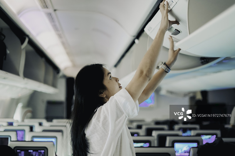 女乘客尝试将行李放入飞机顶部的行李舱内，需要帮助图片素材