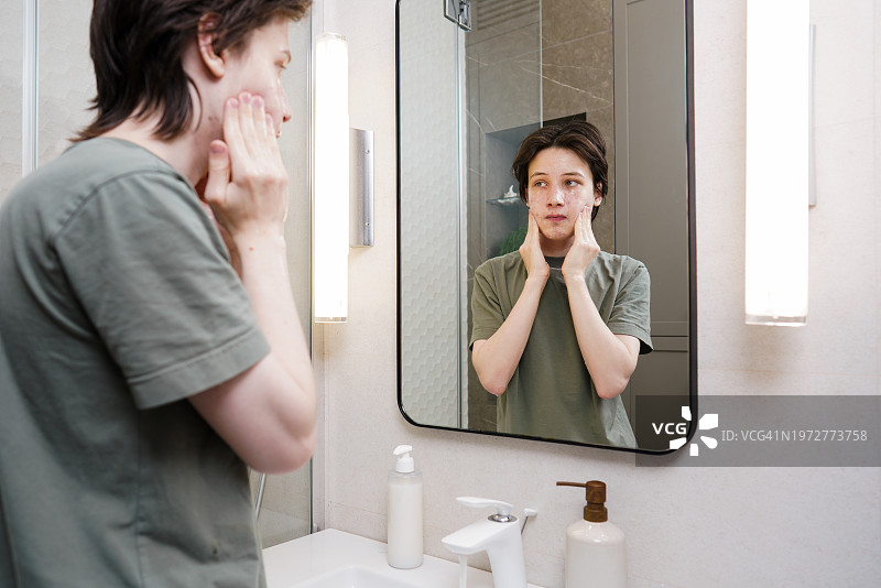 青少年男孩在浴室镜子前用泡沫洗脸，有痤疮皮肤问题。皮肤护理。个人皮肤护理概念。图片素材
