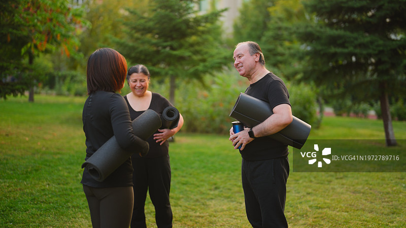 老年夫妇拿着瑜伽垫与教练在户外会面图片素材