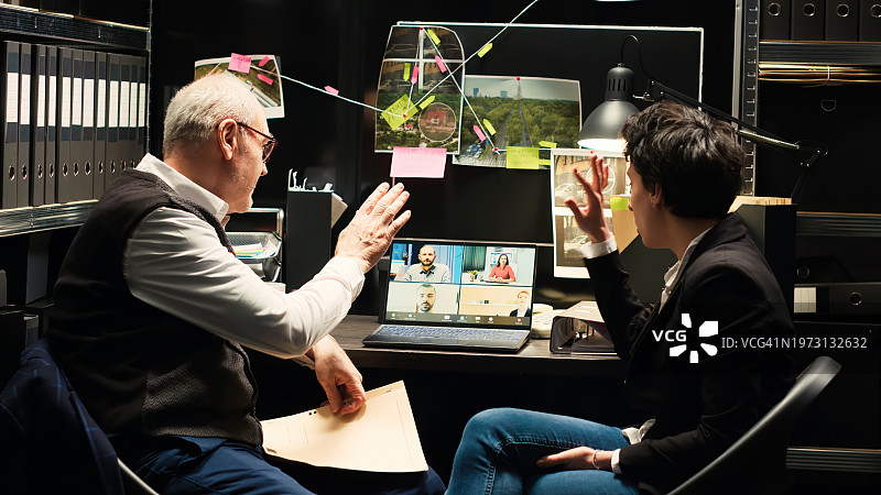 黑暗房间里，两人在桌旁调查，同事在笔记本电脑上协助图片素材