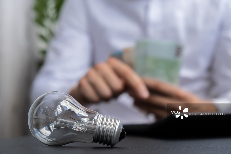 坐在办公桌前手持灯泡的商人（腰部以上）图片素材