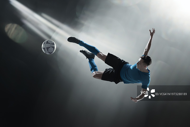 蓝色队服足球运动员在灯光下踢球图片素材