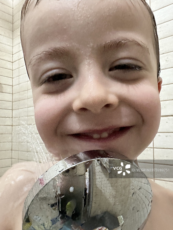 淋浴后，一个三岁男孩洗着脸，带着有趣的意图看着镜头图片素材