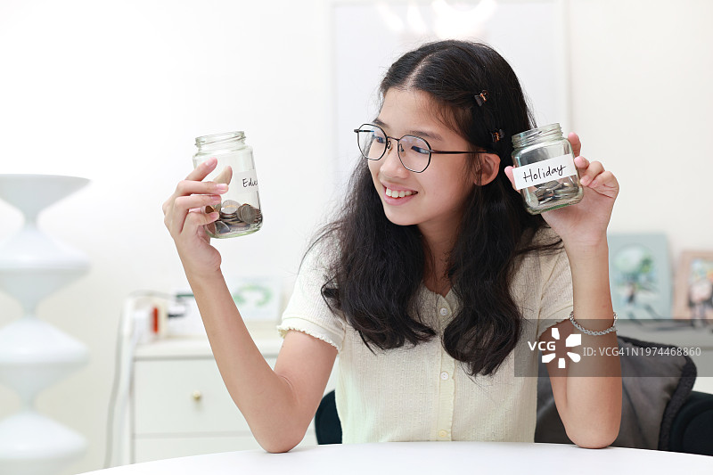 年轻亚裔女孩存钱罐储蓄，为教育和未来假期做准备图片素材