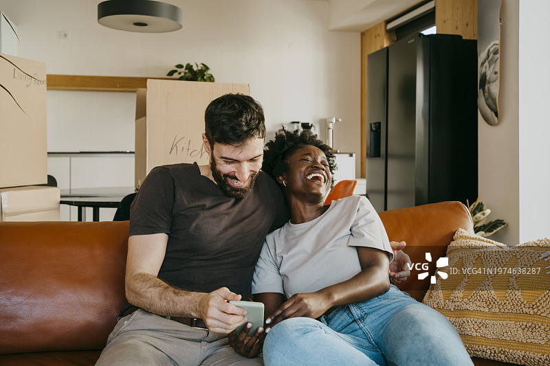 快乐的跨种族夫妇在客厅沙发上分享智能手机图片素材