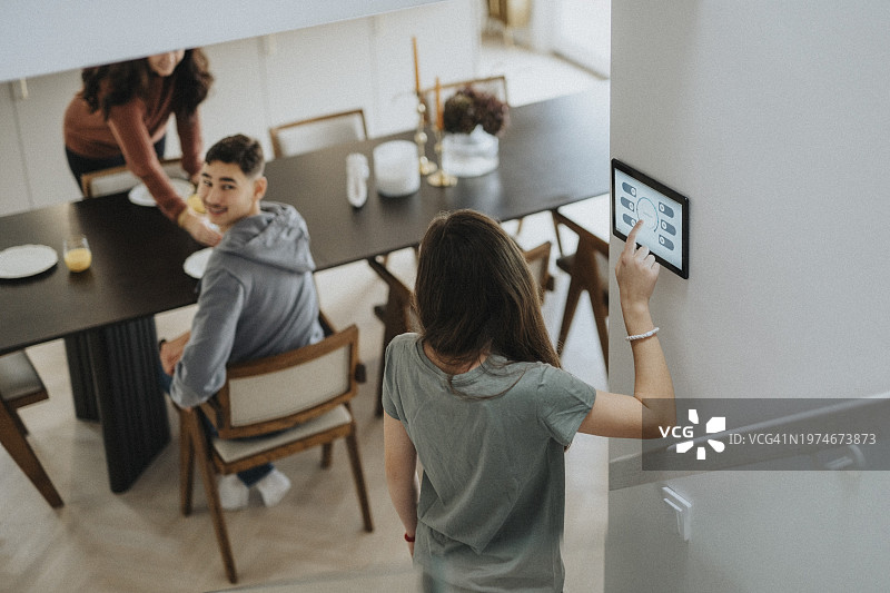 在家中使用安装在墙上的平板电脑与兄弟交谈的女孩图片素材