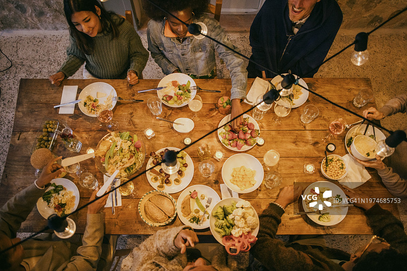 晚餐派对期间坐在照明餐桌旁的多民族朋友的俯视图图片素材