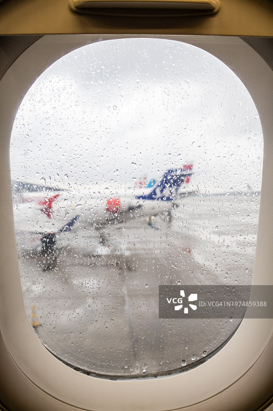从被雨水覆盖的飞机舷窗看到的机场跑道图片素材