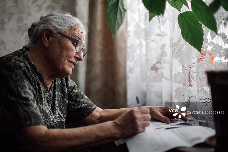 坐在窗前计算账单费用的疲惫老妇人图片素材