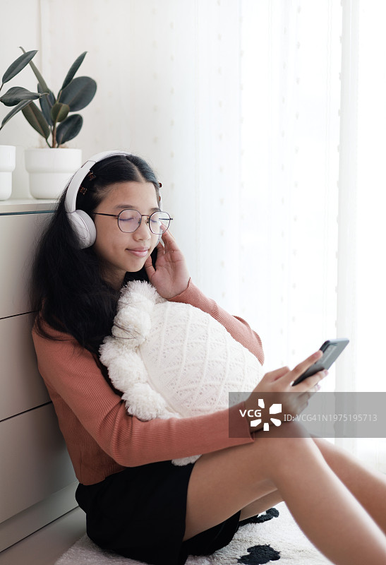 亚洲小女孩在家用手机耳机听音乐。图片素材