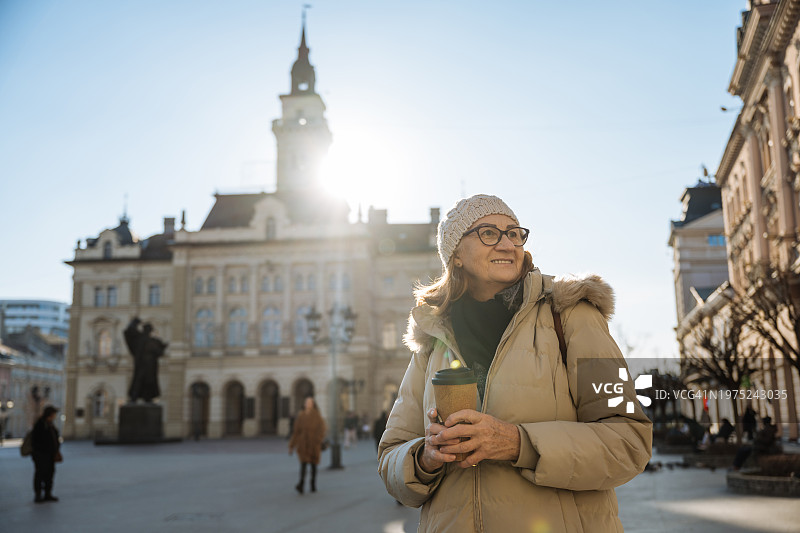 城市休闲游：手拿咖啡享受阳光午后的年长女性图片素材