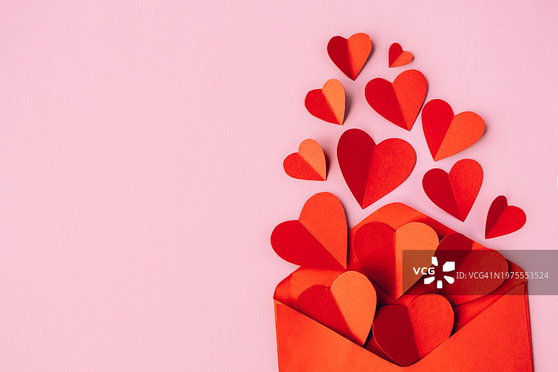 粉红色背景上带有纸质心形的红色红包。情人节，爱心概念图片素材