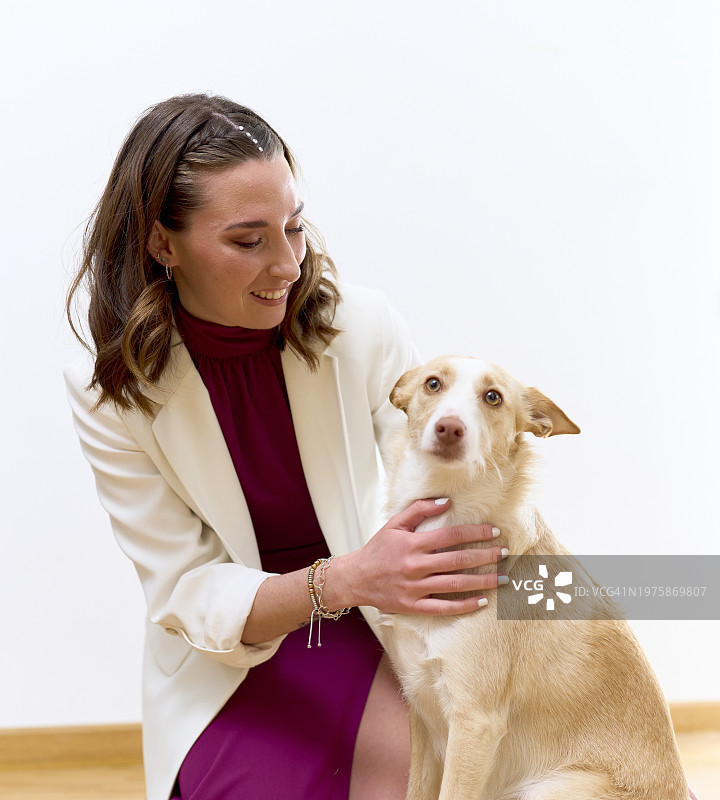 漂亮的白人女孩穿着半正式的衣服，抚摸着她的狗，面带微笑。图片素材