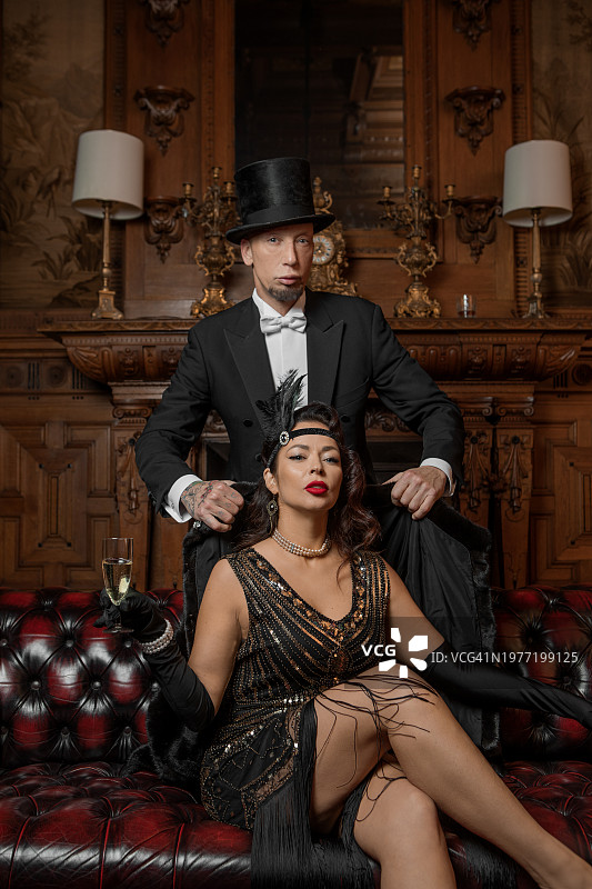 豪宅中穿着奢华的1920年代风格的漂亮黑发女子与男性陪伴者图片素材