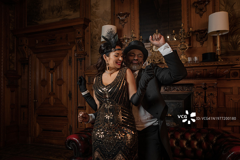 豪宅中穿着奢华的1920年代风格的漂亮黑发女子与男性陪伴者图片素材