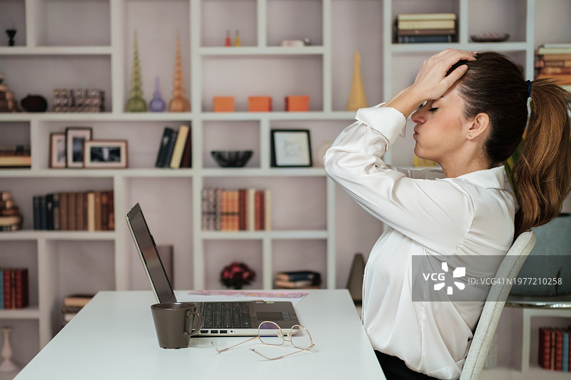 沮丧的女程序员坐在办公室里，双手抱头图片素材