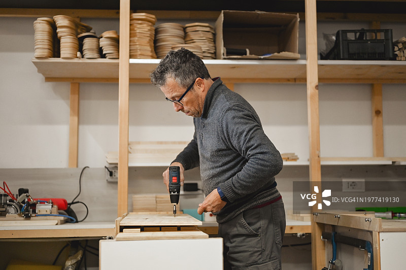 侧面视角：成熟男子在车间用电钻钻木板图片素材