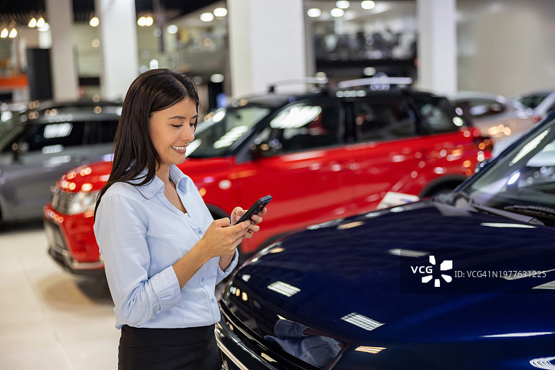 在汽车经销店工作的女商人用手机发短信图片素材