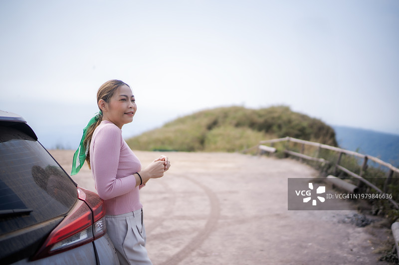 靠在车上，面带微笑看向山景的亚洲女性图片素材