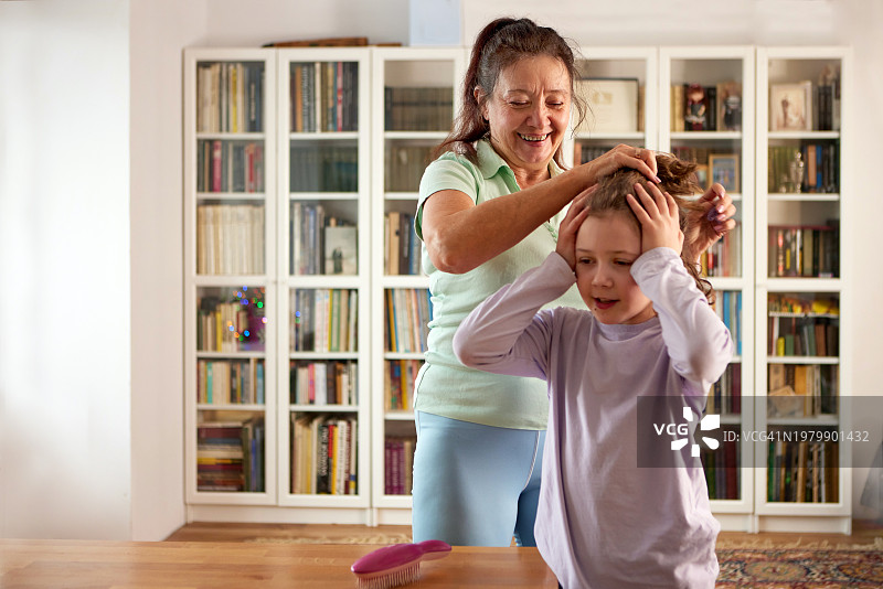 奶奶在家中书柜前为孙女梳头图片素材