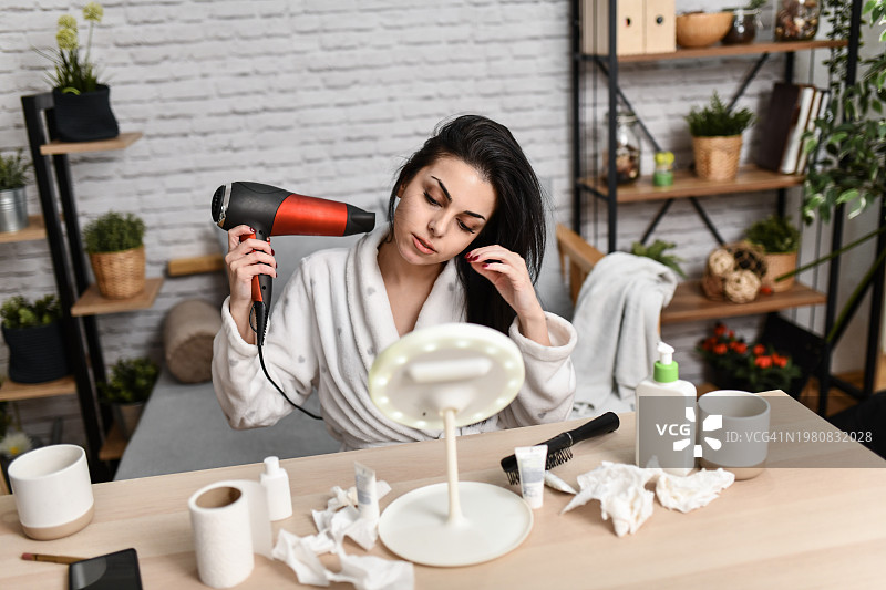 浴后女子在镜子前用风扇吹干头发图片素材