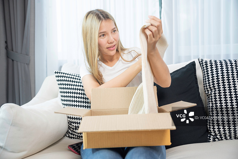 坐在沙发上打开包裹的兴奋的年轻亚洲女性图片素材
