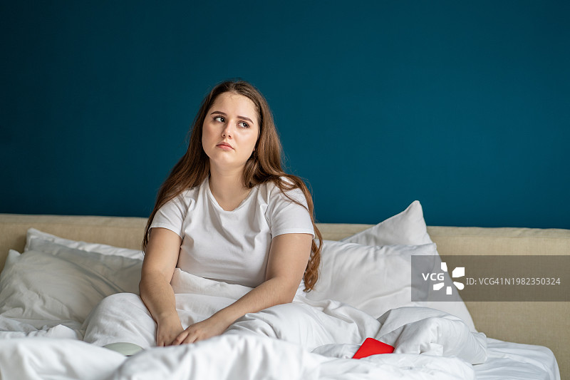 早上因长期睡眠不足而坐在床上的年轻女子图片素材