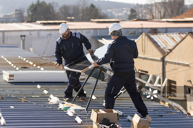 技师搬运光伏太阳能组件，同时在房屋屋顶上安装太阳能电池板系统图片素材