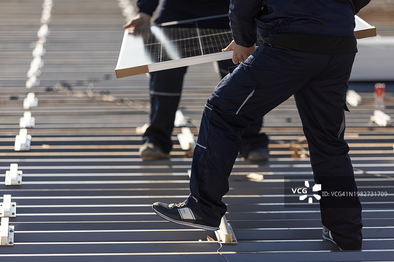 技师搬运光伏太阳能组件，同时在房屋屋顶上安装太阳能电池板系统图片素材