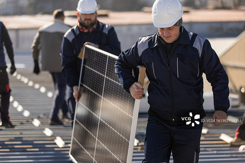 技师搬运光伏太阳能组件，同时在房屋屋顶上安装太阳能电池板系统图片素材