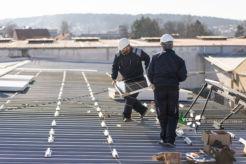 技师搬运光伏太阳能组件，同时在房屋屋顶上安装太阳能电池板系统图片素材