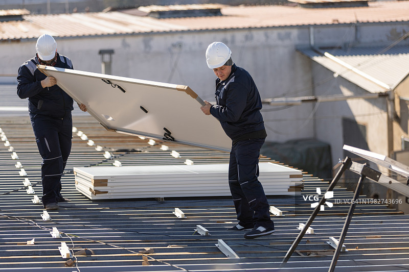 技师搬运光伏太阳能组件，同时在房屋屋顶上安装太阳能电池板系统图片素材