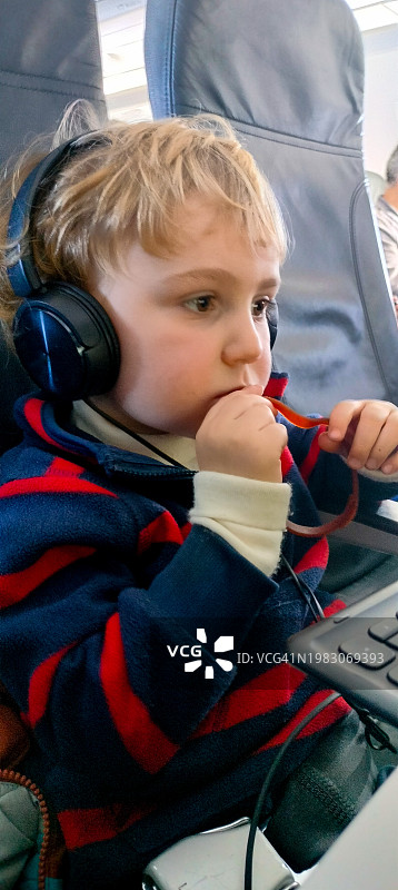 戴着耳机在飞机座位上看电脑的金发儿童图片素材
