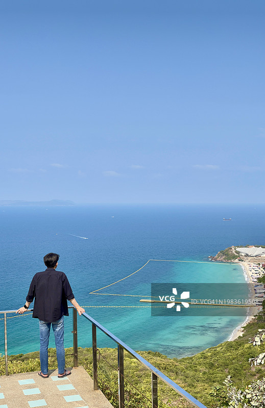 穿着黑色衬衫和牛仔裤的男人独自站在芭堤雅阁兰岛观景点的悬崖上，欣赏美丽的大海和晴朗的蓝天，泰国图片素材