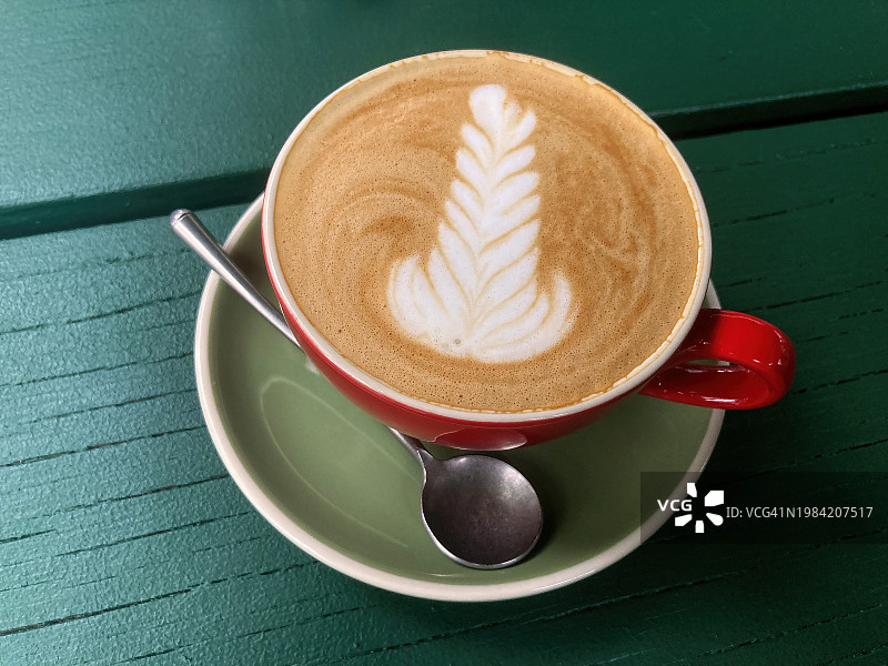 在深绿色野餐桌上，红色陶瓷杯和橄榄绿茶托盛放的馥芮白咖啡图片素材