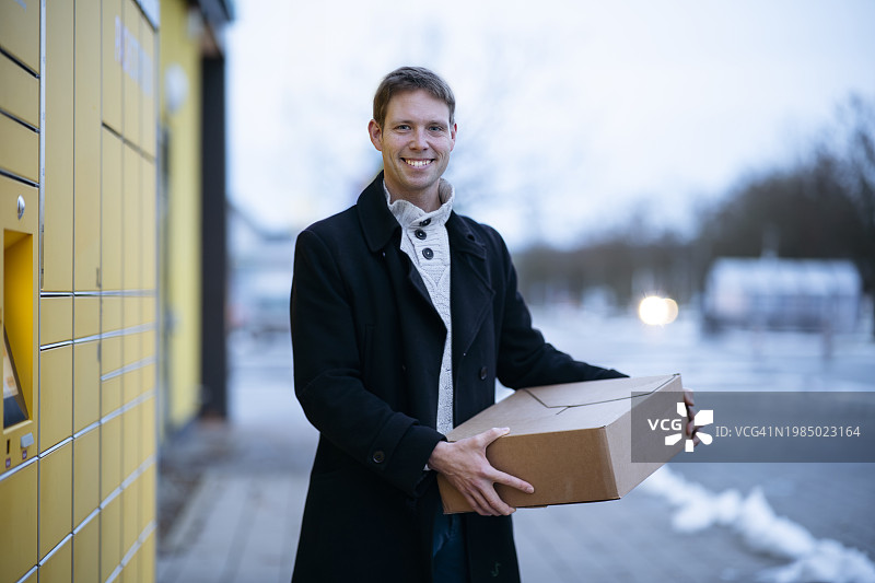 在包裹柜附近拿着包裹盒的快乐男人图片素材