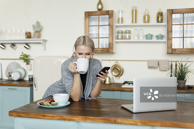 年轻女人在家喝咖啡并使用智能手机图片素材