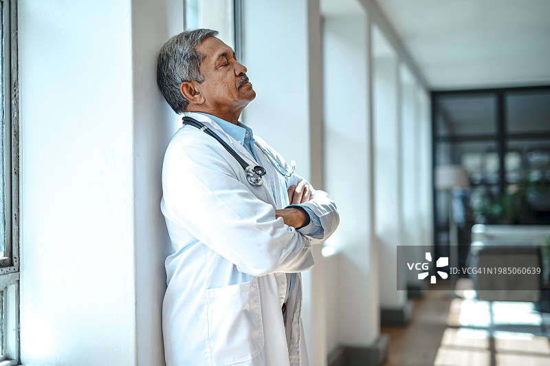 年长的男医生在医院休息室手臂交叉靠在柱子上的侧面视角图片素材