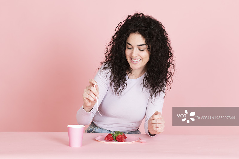 快乐的年轻女人在桌旁拿着草莓和咖啡杯图片素材